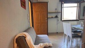 Ein Zimmer mit braunem Sofa, einer Holztür, einem Esstisch mit Stühlen und einem Fenster mit Aussicht.