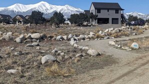 A modern two-story house with a garage, surrounded by a rocky landscape and snow-capped mountains in the background.