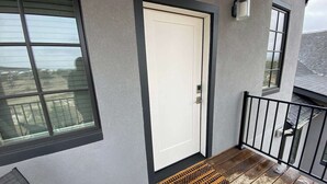 A residential entryway with a white door, a small porch with a wooden floor, and a black metal railing.