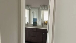 A narrow hallway leading to a bathroom with a white door, a dark floor, and a tiled floor.