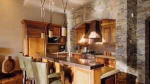 Una cocina con una pared de acento de piedra, armarios de madera, una isla central con taburetes de bar e iluminación colgante.