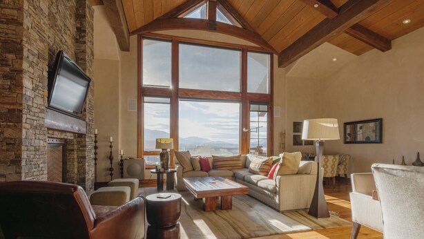 Un salón amplio con chimenea de piedra, ventanas grandes y vigas de madera.