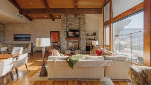 Un salón espacioso con chimenea de piedra, vigas de madera en el techo y grandes ventanas con vistas a la ciudad.