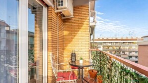 Un balcon avec un mur en briques, une porte vitrée, une petite table avec une chaise et des plantes en pot.