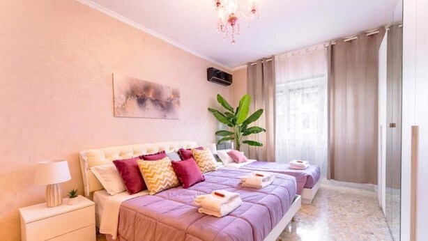 Une chambre à coucher avec un grand lit, une table de chevet, une plante en pot et une fenêtre avec des rideaux.