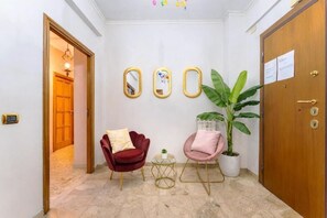 A hallway with a wooden door, a red chair, a pink chair, a small table, and a potted plant. - 7th Floor Terrace Stay - San Giovanni & Colosseum (Roma)