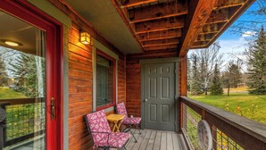 Un portico in legno con una porta rossa, due poltrone decorate e un tavolino.