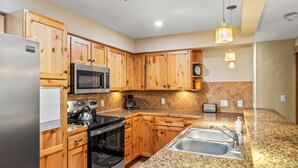 Una cucina moderna con mobili in legno, elettrodomestici in acciaio inossidabile, piani di lavoro in granito e illuminazione a sospensione.