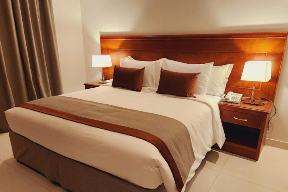 A hotel room with a large bed, two bedside tables, a wooden headboard, and a nightstand with a lamp.