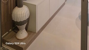Una sala de estar moderna con un televisor de pantalla plana montado en una pared blanca, un mueble de madera debajo y un jarrón decorativo con ramas.