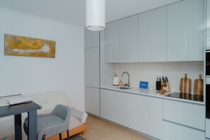 Una cocina moderna con armarios blancos, un lavamanos de acero inoxidable y una encimera con utensilios básicos.