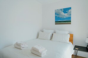 A hotel room with a bed, pillows, a nightstand, and a painting of a beach scene.