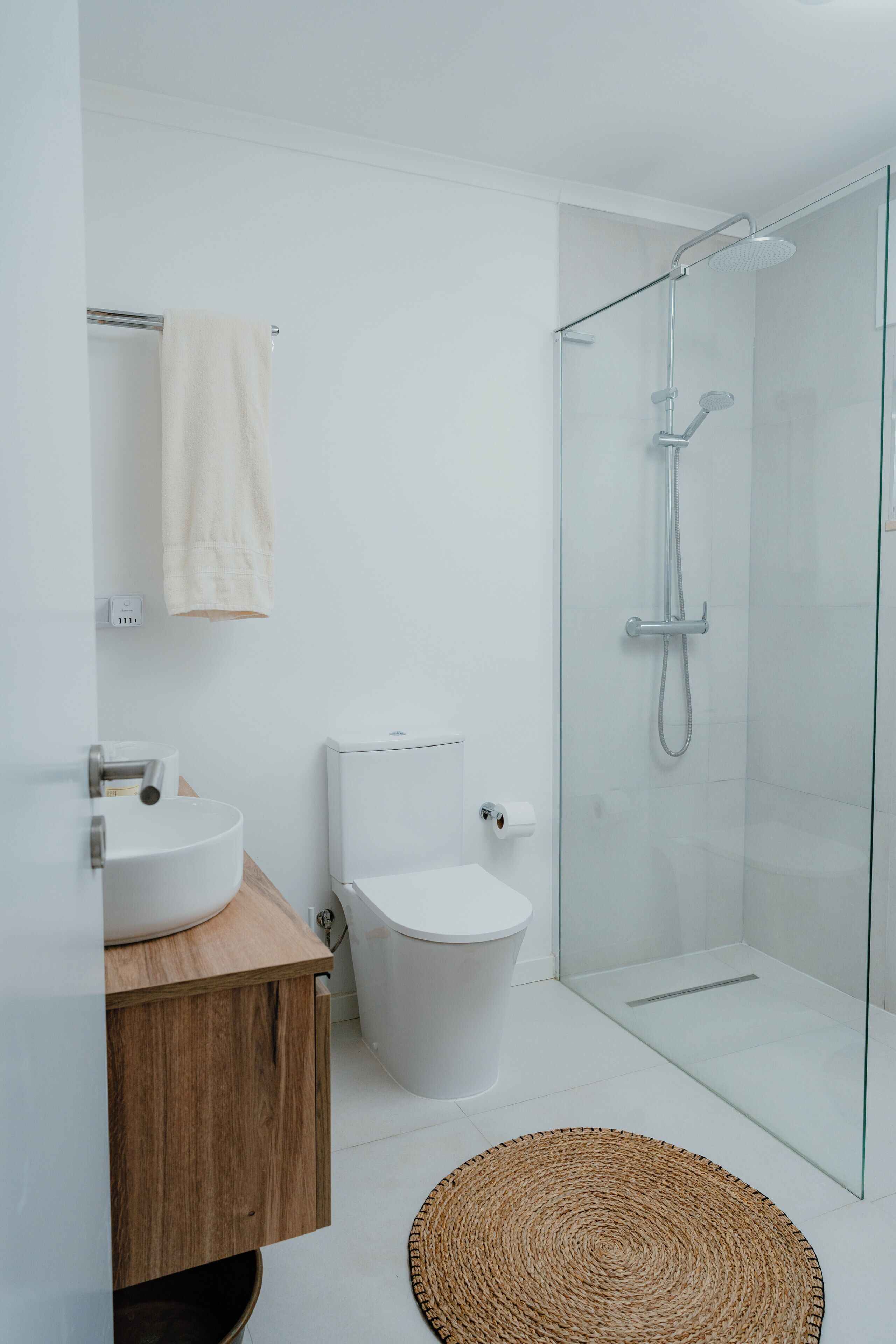 A modern bathroom with a glass shower enclosure, a white toilet, and a wooden vanity with a sink.