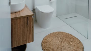 A modern bathroom with a glass shower enclosure, a white toilet, and a wooden vanity with a sink.