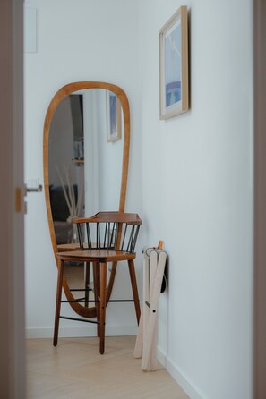 A room with a wooden chair and table, a mirror, and a framed picture on the wall.