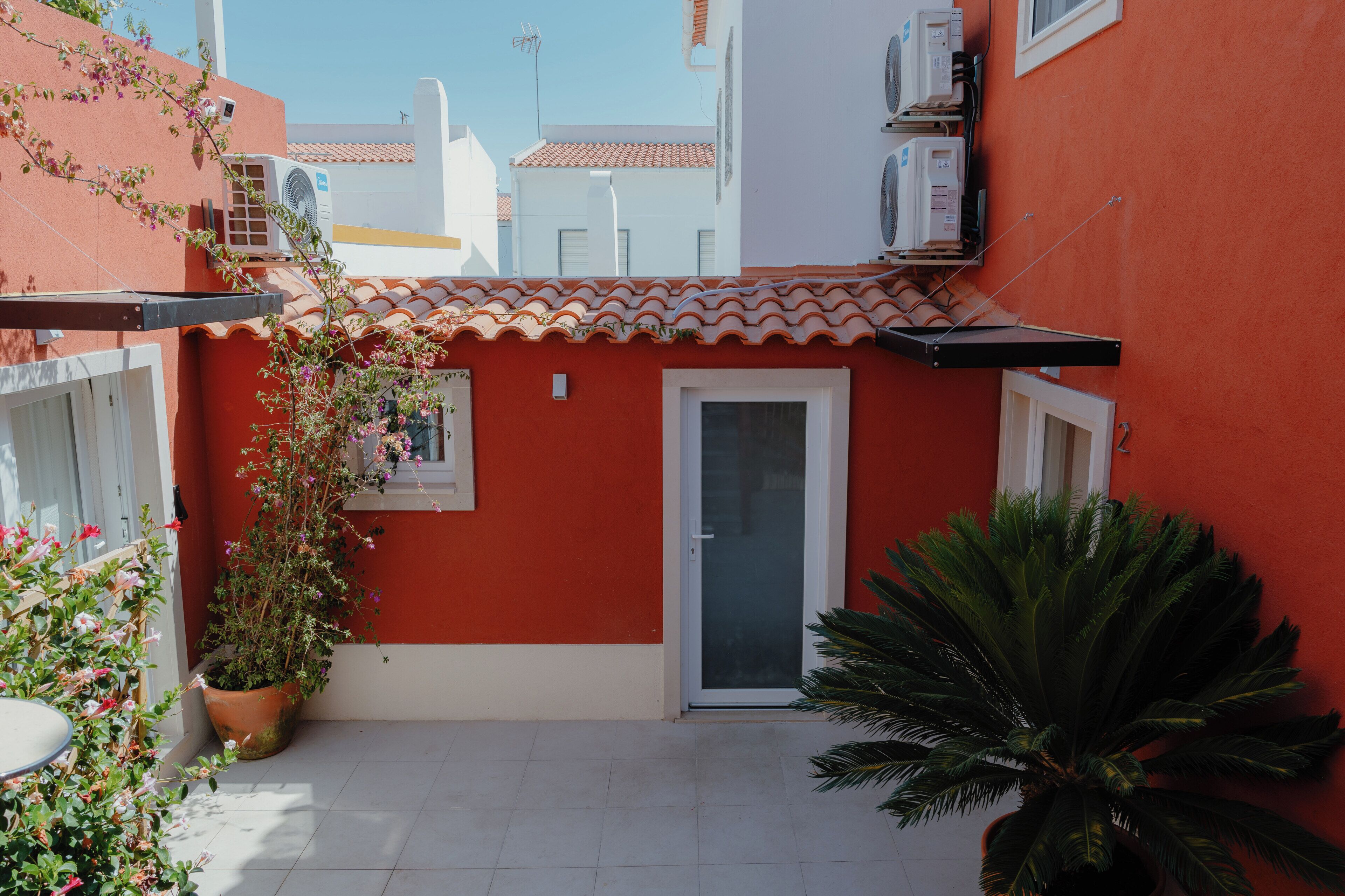 Un patio con un muro rojo, una puerta blanca y una planta en maceta.