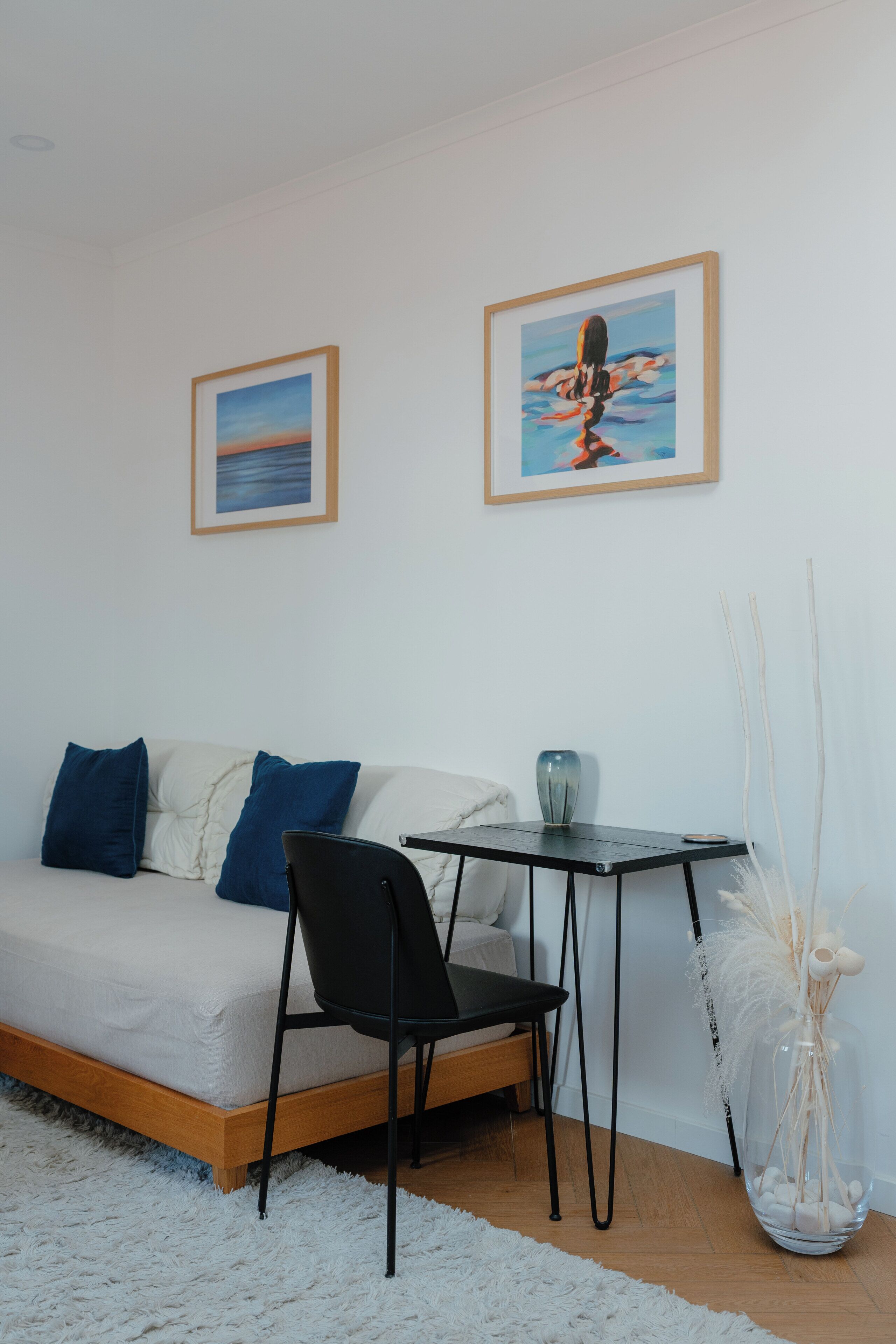 A modern living room with a sofa, a black chair, a small table, and two framed artworks on the wall.