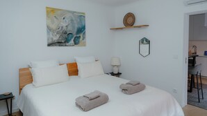 Ett hotellrum med en säng, kuddar, ett sängbord, en lampa, en tavla och en liten hylla med en dekorativ prydnad.