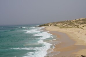 A beach with waves, a sandy shore, and a hilly landscape in the background. - Kalumi Aparthotels (Odemira)