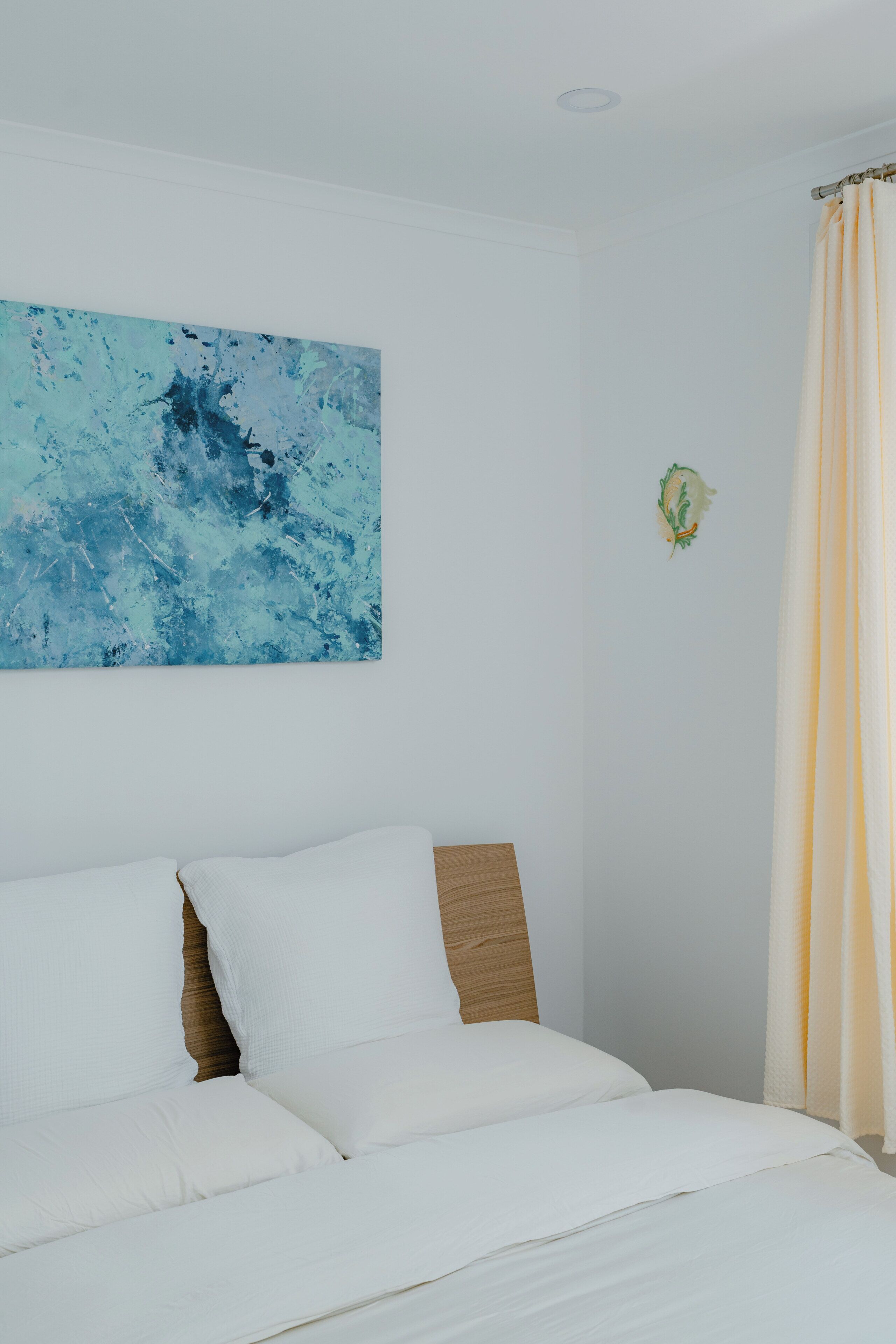 A bedroom with a bed, a headboard, a wall-mounted artwork, and a curtain.