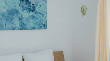 A bedroom with a bed, a headboard, a wall-mounted artwork, and a curtain.