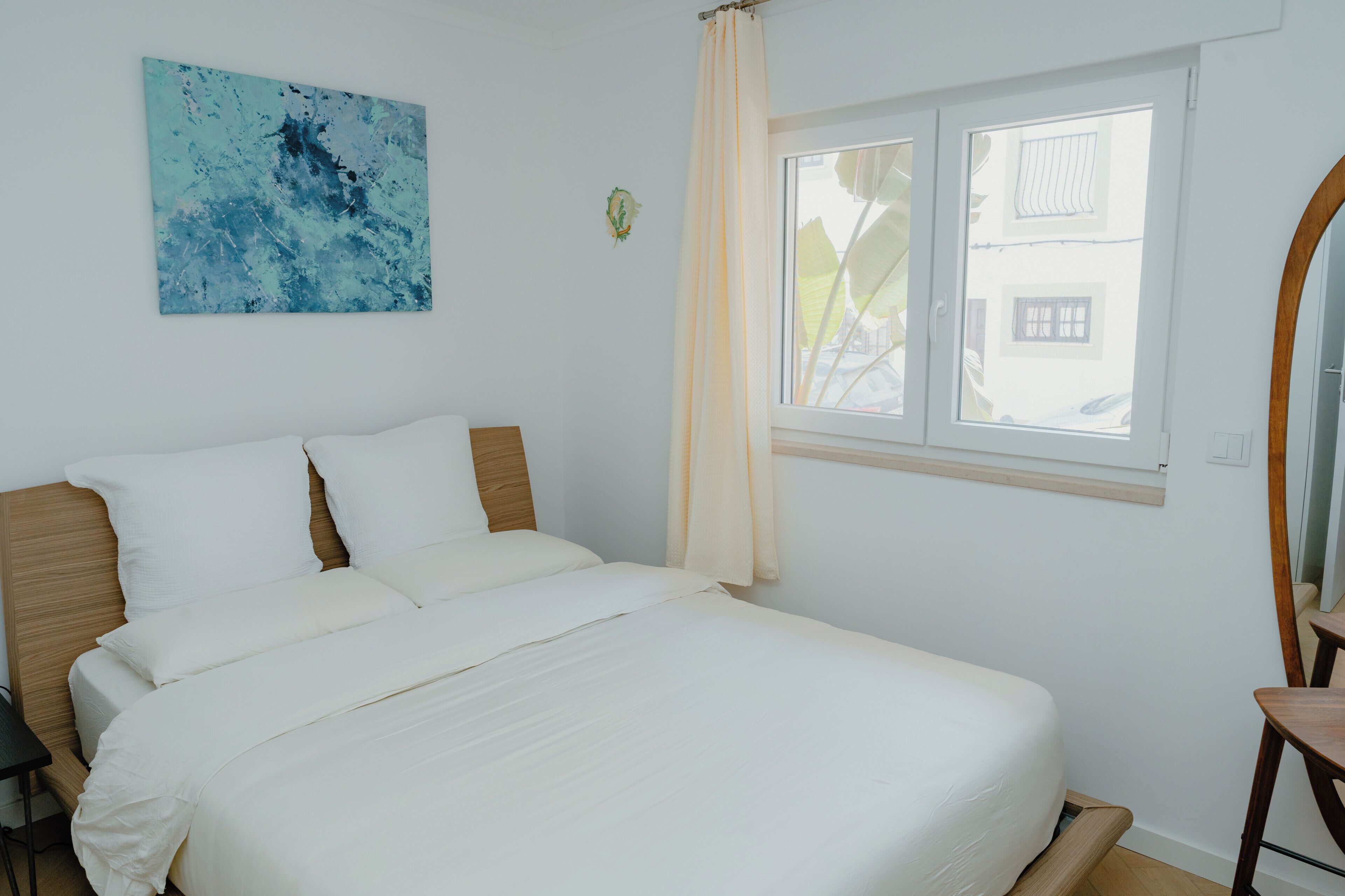 A bedroom with a bed, a window, a painting, and a chair.