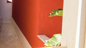 Un estrecho callejón con un muro rojo y una verja blanca. Se ve un letrero en la pared con el número '6' y el nombre 'Kalumi'.
