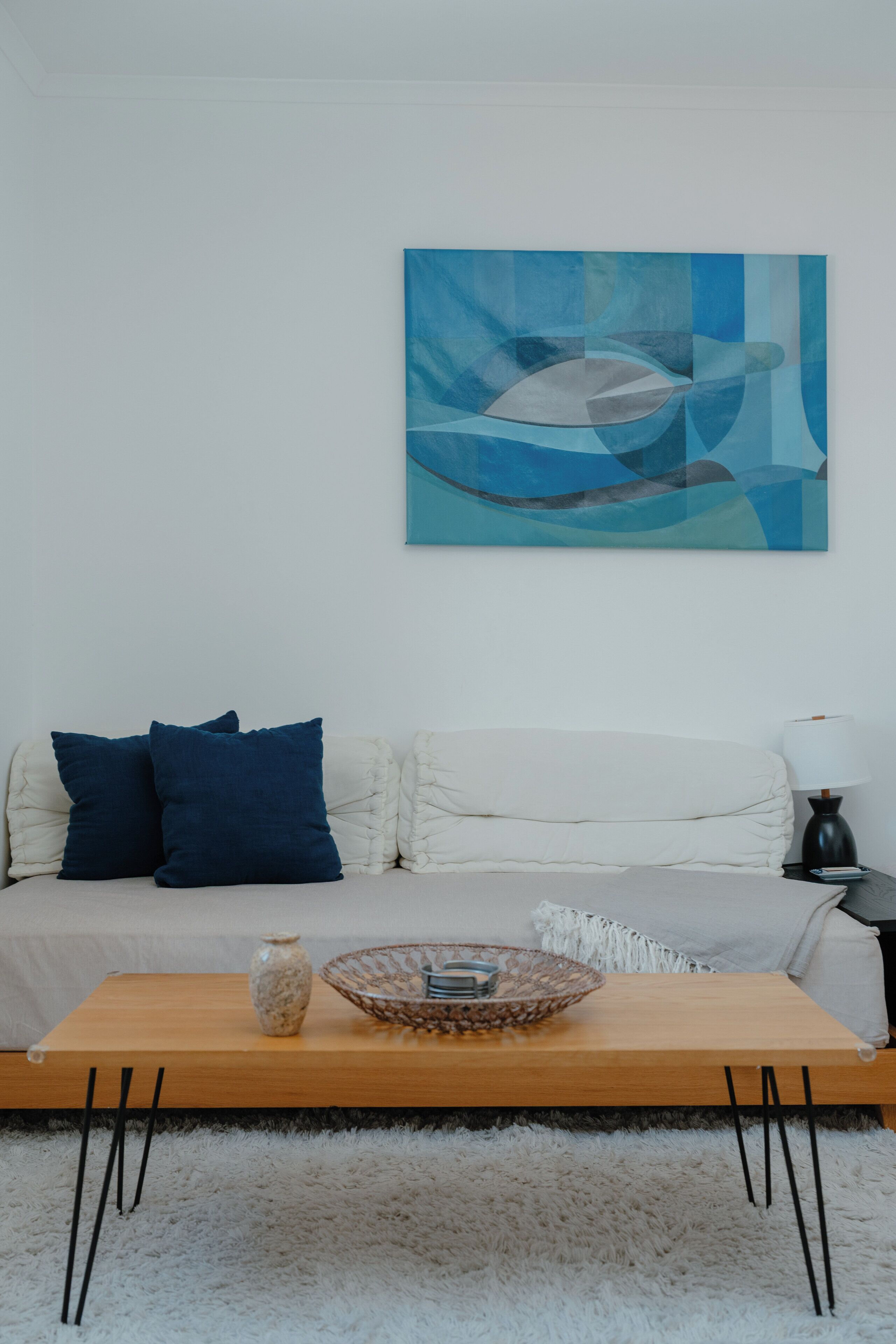 A modern living room with a sofa, cushions, a coffee table, a vase, and a wall art piece.