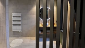 A modern bathroom with a large mirror, a towel rack, and a wooden floor. - La Suite   (Roanne)