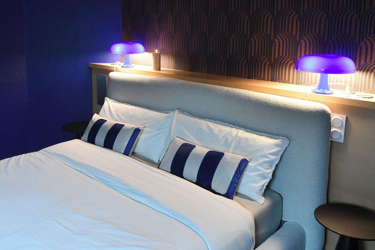A neatly made bed with white and blue striped pillows, a grey headboard, and two bedside lamps with blue lighting.
