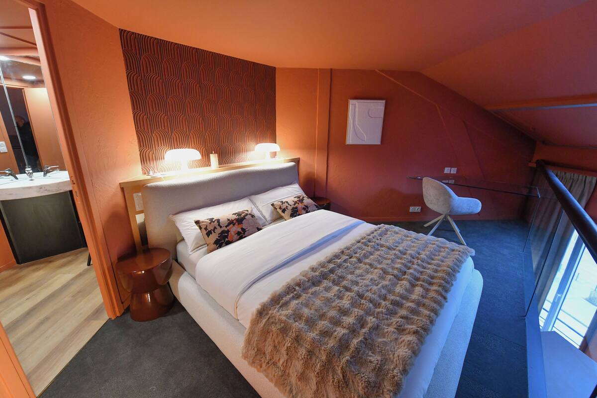 A hotel room with a bed, bedside table, lamp, and a chair.