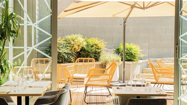 An outdoor dining area with tables and chairs, a large umbrella, and potted plants. - La Suite   (Roanne)