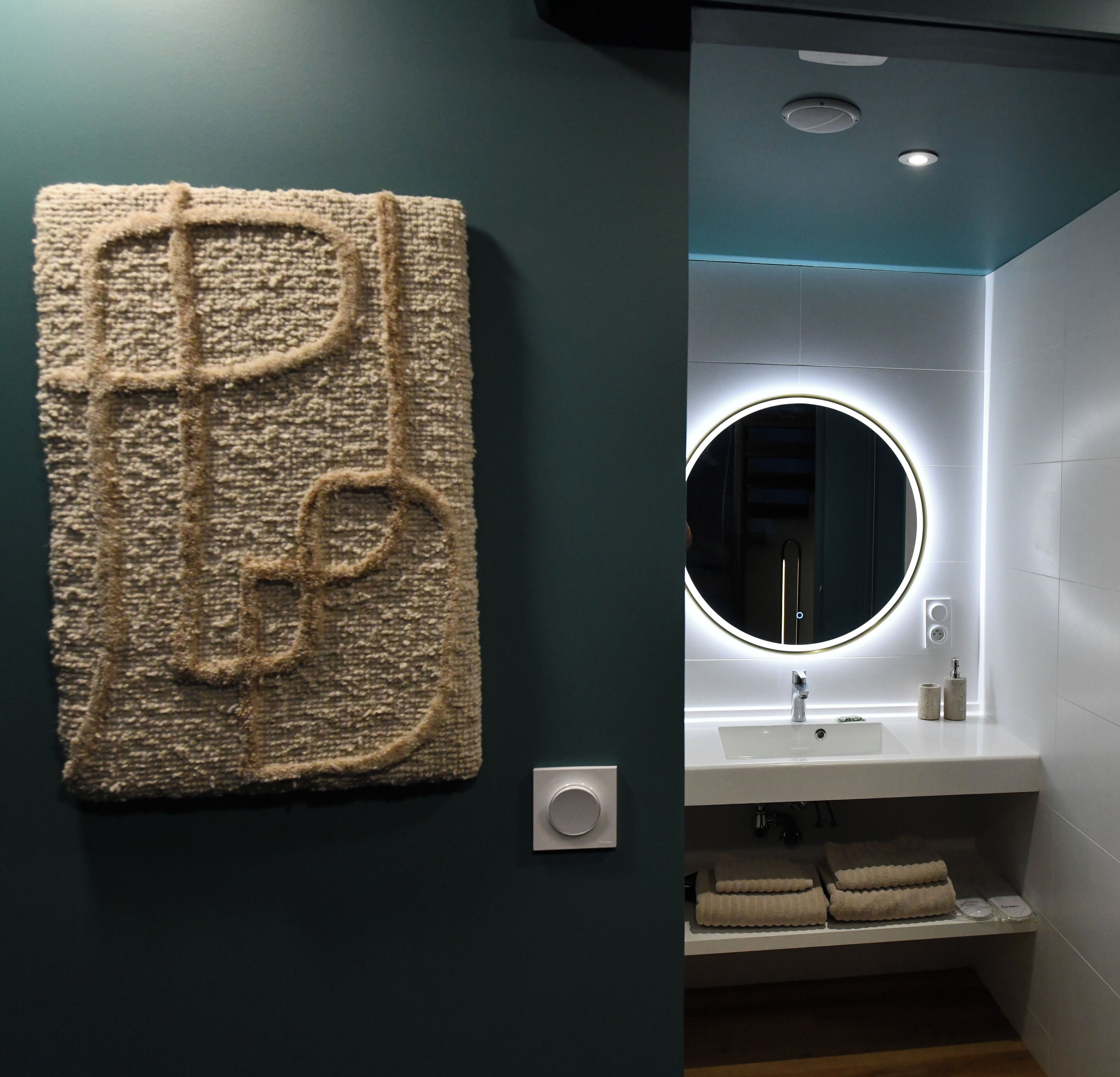 A bathroom with a modern design, featuring a large wall-mounted mirror, a sink, and a towel rack.