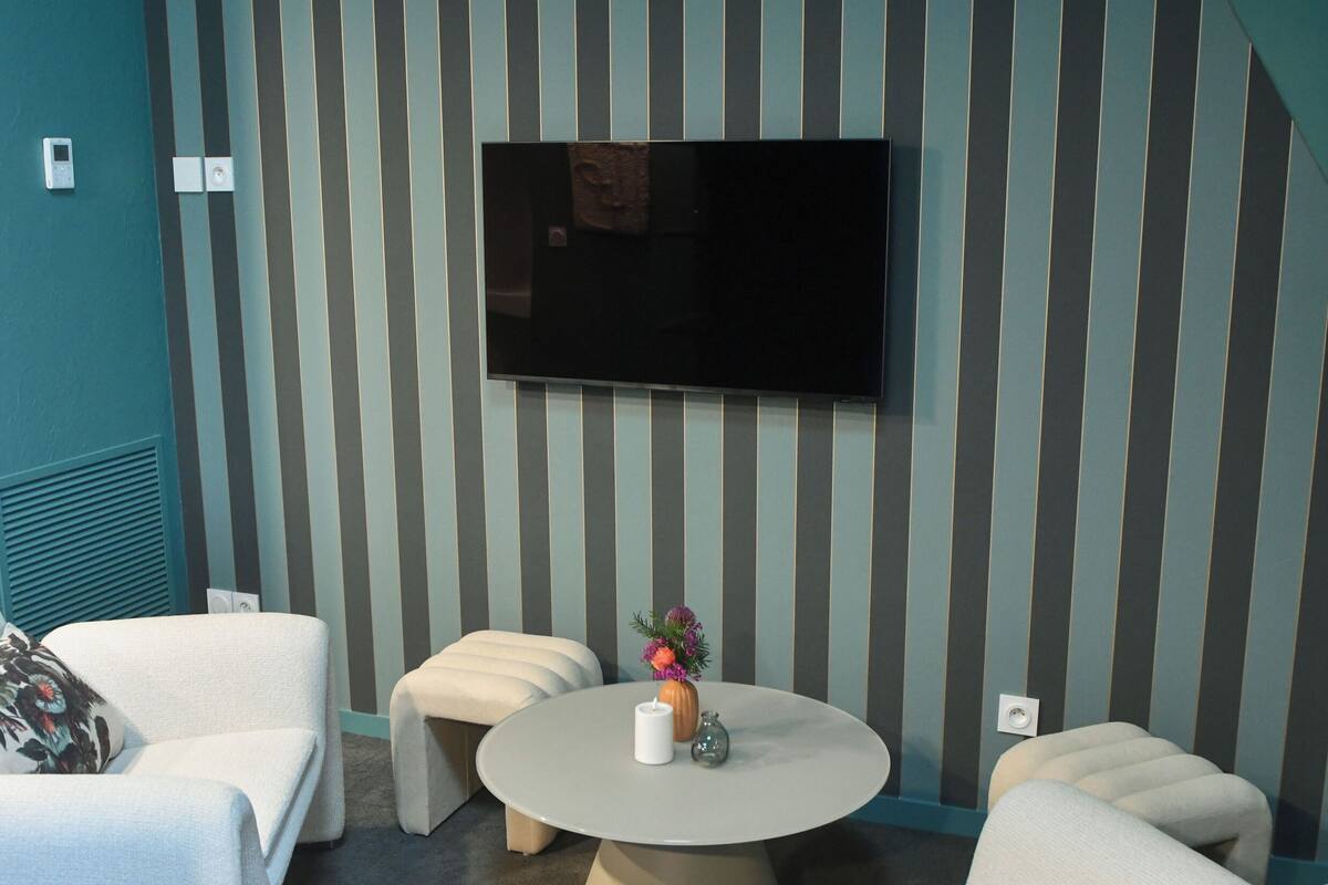 A modern living room with a flat-screen TV mounted on the wall, a round coffee table, and two white sofas.