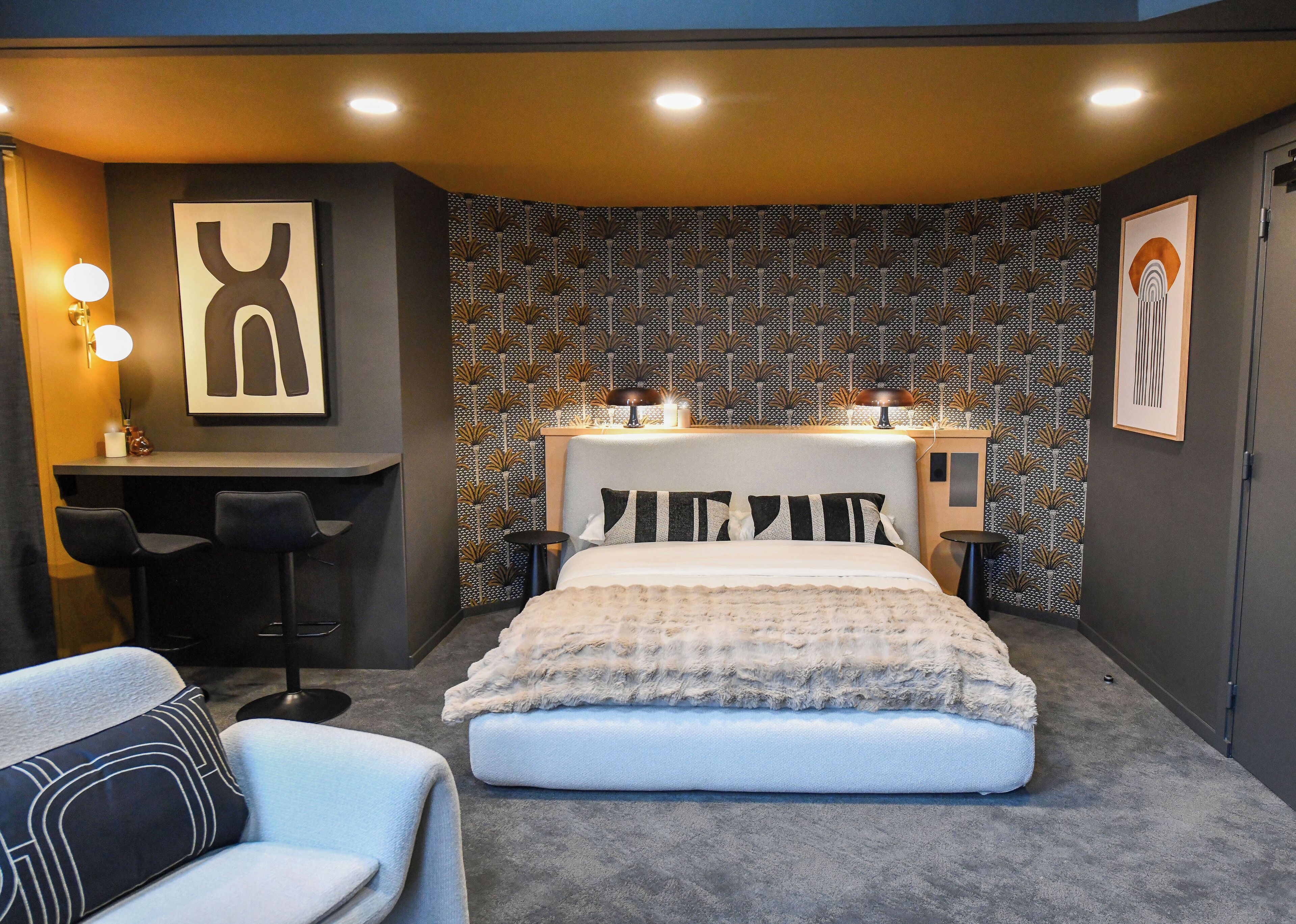 A modern bedroom with a large bed, a desk with two chairs, and a patterned wallpaper.