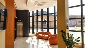 A spacious lobby with a modern design, featuring a large window, a flat-screen TV mounted on the wall, and a potted plant. - La Suite   (Roanne)