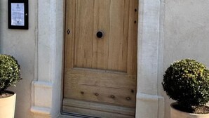 Una puerta de madera con diseño sencillo, flanqueada por dos macetas y una pequeña placa en la pared.