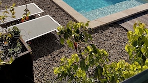 Una piscina rectangular con agua azul cristalina, rodeada de una solera de piedrecitas y equipada con sillas de descanso.