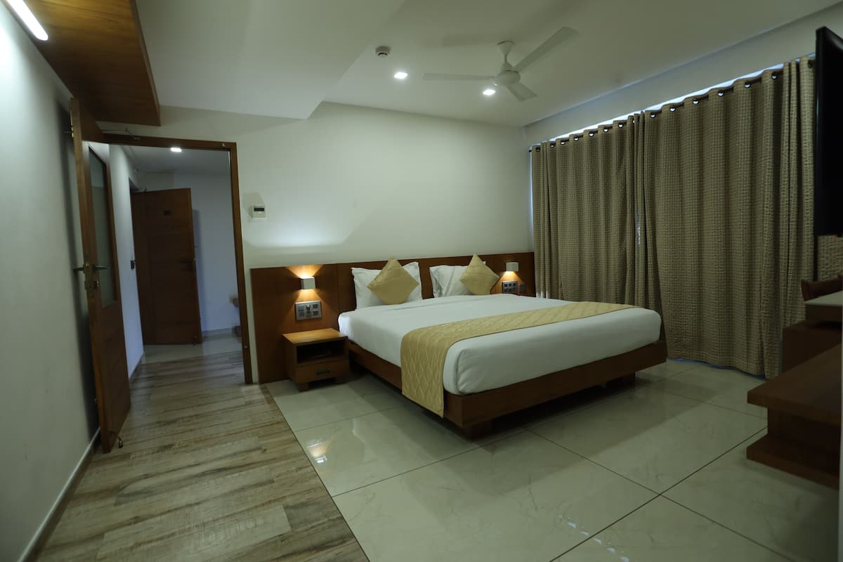 A hotel room with a large bed, wooden headboard, bedside lamps, a ceiling fan, and a view of the outside through curtains.