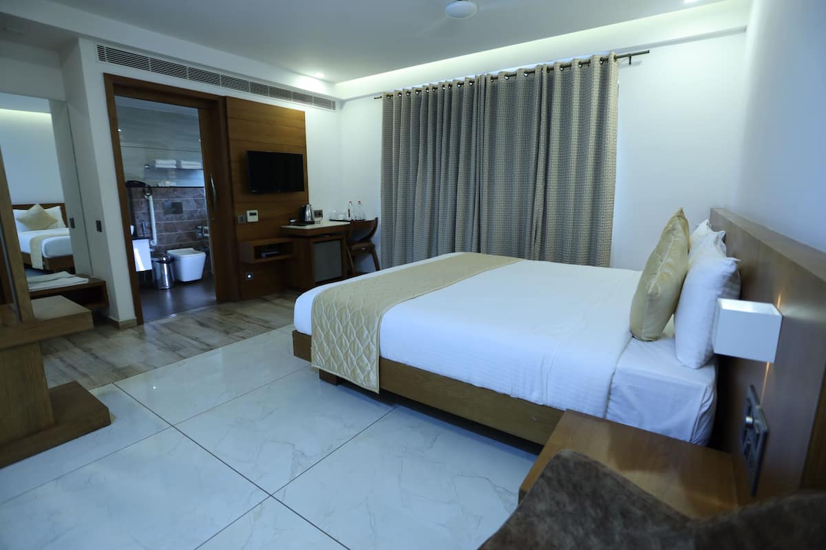 A hotel room with a large bed, a desk, a chair, a TV, and a bathroom visible through an open door.