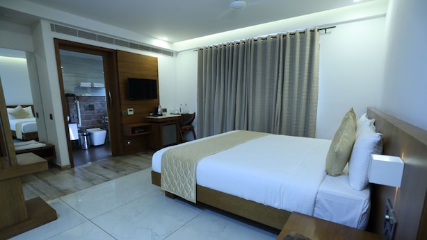 Ein Hotelzimmer mit einem großen Bett, einem Schreibtisch, einem Sessel, einem Fernseher und einem durch eine offene Tür einsehbarer Badezimmer.