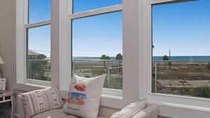 Ein Zimmer mit großen Fenstern und Blick auf den Strand, inklusive Sitzkissen mit Strandmotiv.