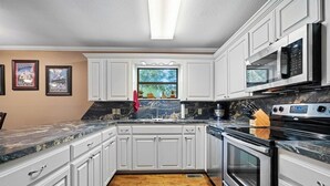 Cocina con gabinetes blancos, encimera negra y electrodomésticos de acero inoxidable.