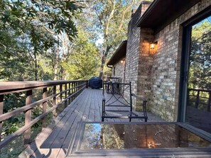 A wooden deck with a glass floor leading to a building with a brick exterior and large windows. - A beautiful modern home nestled in a private wooded setting, 5mins from downtown (Hot Springs)