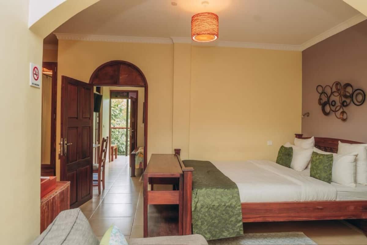 A bedroom with a bed, a wooden table, a bench, and a door leading to another room.