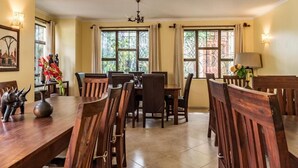 Un coin repas avec une table et des chaises en bois, de grandes fenêtres avec des rideaux et un lustre.