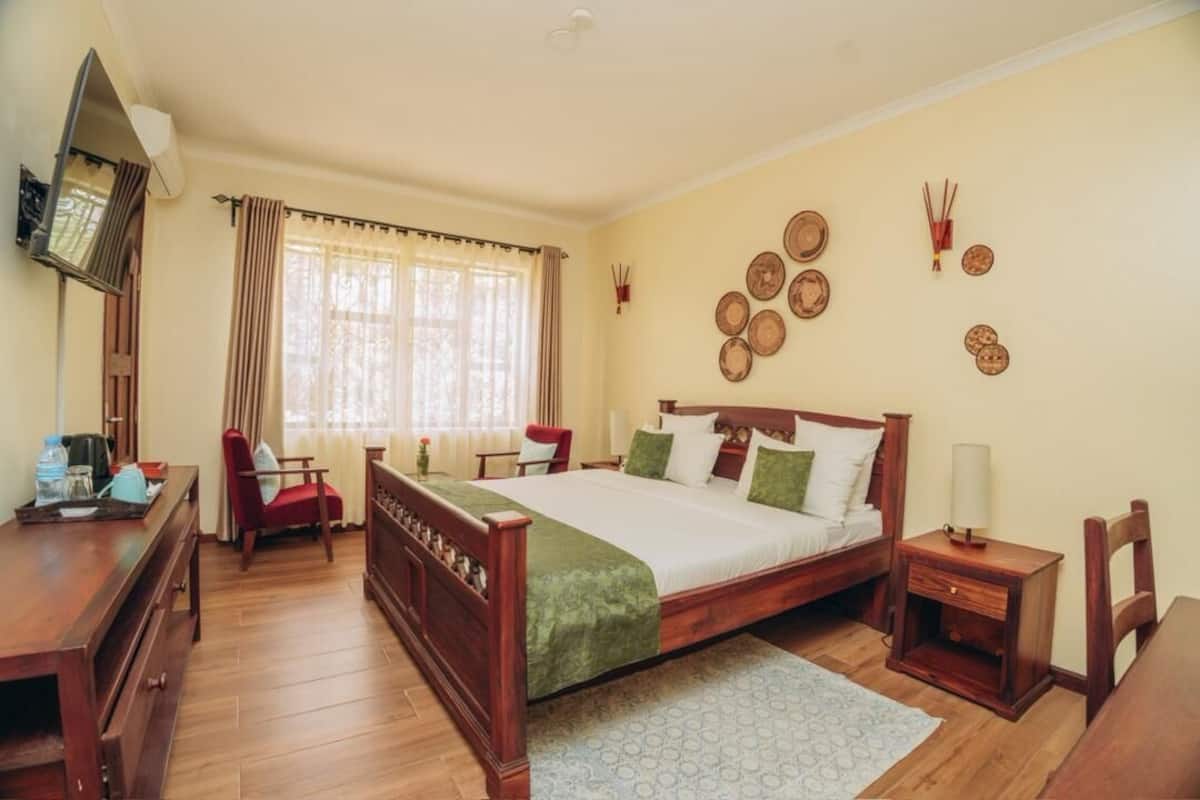 A bedroom with a wooden bed, a desk, a chair, a nightstand, and a window with curtains.