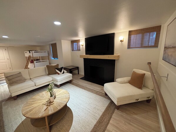 A modern living room with a fireplace, white sofas, a coffee table, and a flat-screen TV mounted above the fireplace.