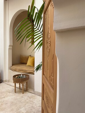 A cozy seating area with a cushioned bench, a small round table with glassware, and a large potted plant. - Riad Al Muhandiz (Marrakech)