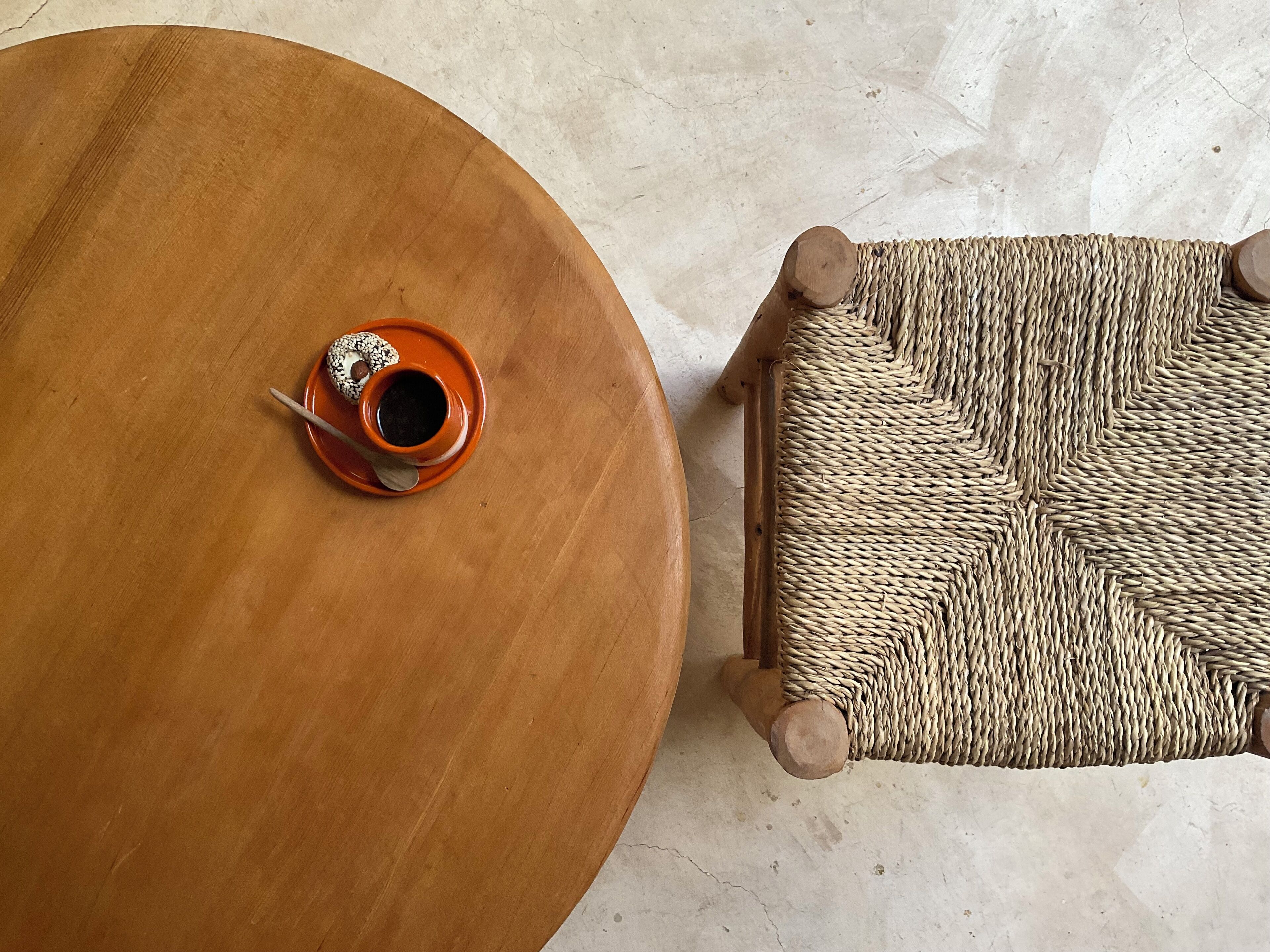 A round wooden table with a woven stool beside it.